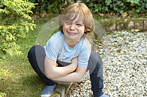Image of a crying little boy who has crawled angrily in a corner of the garden