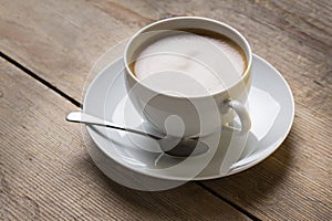 Image of a cup of coffee on a suacer with an old vintage spoon and a vanilla cookie, placed on a wooden table top