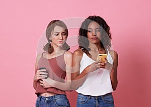 Image of curious woman spying and peeking at smartphone of her friend isolated over pink background
