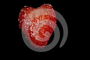 Cut slice of a red juicy strawberry covered in sugar crystalls on a black background photo