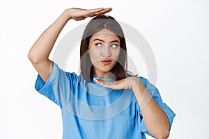 Image of cute brunette girl putting her head and face in frame, looking away and pucker lips silly, standing in blue