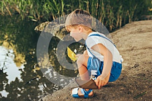 Image of cute little boy launch paper ship on the lake in the park. Adorable kid boy playing with a boat. Curious child sailing a