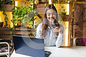 Image of cute pretty young woman sitting in cafe holding glass and drinking wine. portrait of a beautiful wine tasting tourist