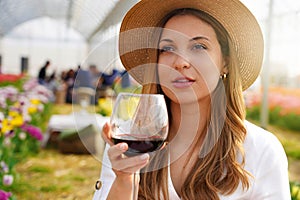 Image of cute young woman enjoying sitting outdors in park holding glass drinking wine