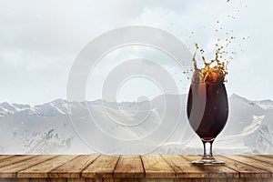 Image of dark foamy beer, glass on wooden table isolated over snowy mountains