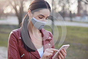 Image of dark haired female with ponytail, standing in yard and holding mobile phone in hands, calls number, looks concentrated,