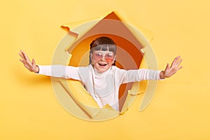 Image of delighted charming cute little girl with braids and in sunglasses wearing casual shirt looking through torn hole in