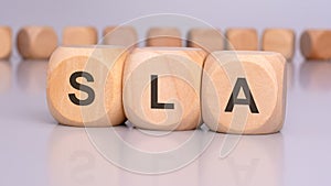 the image depicts three wooden blocks with the letters 'SLA' in focus, reflecting on the table surface. in the