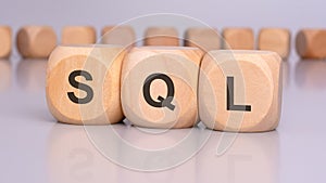 the image depicts three wooden blocks with the letters 'SQL' in focus, reflecting on the table surface. in the