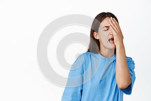 Image of devestated brunette girl slap face, facepalm frustrated, failure emotion, standing over white background