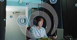 Image of digital padlocks over african american man working on laptop in server room