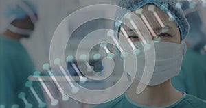 Image of dna strand over portrait of smiling asian female surgeon in operating theatre
