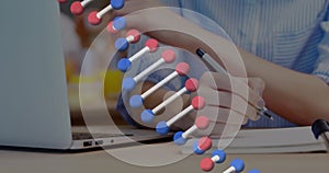 Image of dna strand spinning over businesswoman using laptop