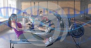 Image of dna strands over diverse women training on rowing machines at gym