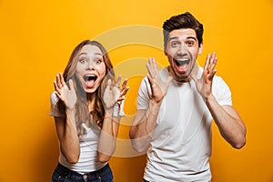 Image of ecstatic people man and woman in basic clothing screaming in surprise or delight and raising arms, isolated over yellow