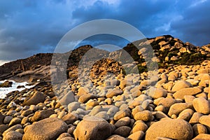 Nature Seascape with Eggshaped Rocks on A Wild Beach and Rocky Mountains at Dramatic Sunrise photo