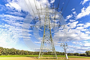 Image of an electricity pylon from the ground perspective in front of a blue sky with white clouds