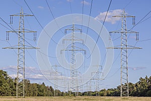 Image of an electricity pylon from the ground perspective in front of a blue sky with white clouds