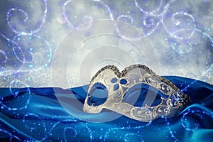 Image of elegant blue and gold venetian mask over blue silk fabric background.