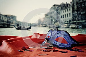 Image of elegant venetian mask on red silk fabric in front of blurry Venice background.
