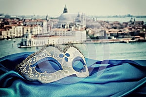 Image of elegant venetian mask on silk fabric in front of blurry