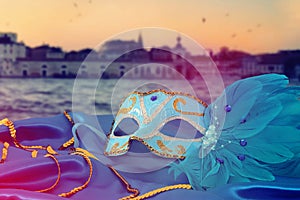 Image of elegant venetian mask on silk fabric in front of blurry Venice background.