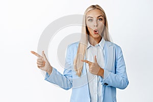 Image of enthusiastic businesswoman pointing fingers left, say wow, showing company advertisement, standing over white