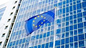 Image of EU flag fluttering on wind against high business office building made of concerete and glass. Concept of