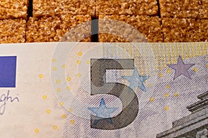 The image of a Euro banknote covering brown sugar, symbolizing the price one pays for indulgence