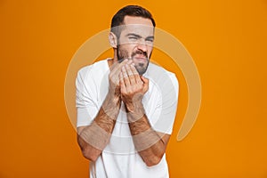 Image of european man 30s in t-shirt touching his cheek and suffering from toothache while,  over yellow background