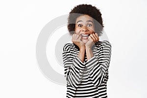 Image of excited african girl gasping in awe, looking surprised and fascinated, watching something amazing happening