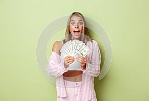 Image of excited girl winning prize, holding money and smiling surprised, standing over green background
