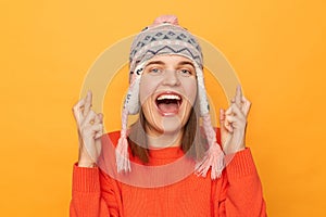 Image of excited happy woman wearing orange sweater and knitted earflap hat standing isolated over yellow background, dreaming
