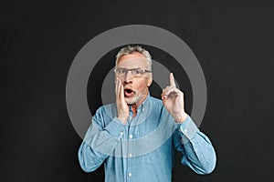 Image of excited retired man 60s with grey hair and beard in shirt shouting in surprise have idea and pointing index finger