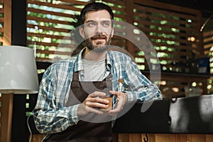 Image of excited waiter boy sitting at the bar while working in cafe or coffeehouse outdoor