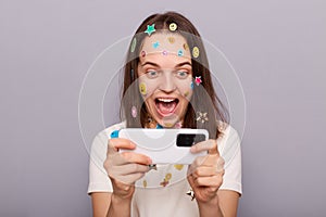 Image of excited woman gamer covered with funny stickers posing isolated over gray background, playing video games, winning level