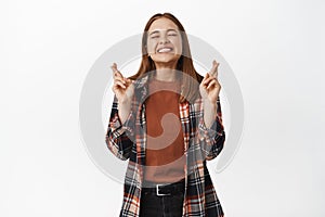 Image of excited woman hoping for smth, cross fingers, smiling with eyes closed, begging fortune to dream come true