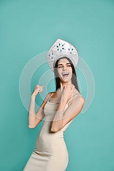 Image of excited young woman in kokoshnik hat standing isolated over blue background make winner gesture.