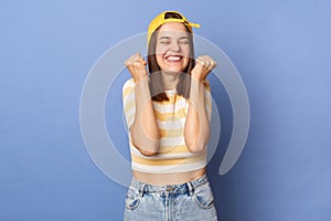 Image of extremely happy joyful teenager girl wearing striped T-shirt and baseball cap posing isolated over blue background,