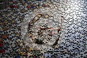 Image of eye glasses casting a shadow on a large group of puzzle pieces