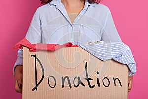 Image of faceless woman wearing blue casual shirt, holding box full of clothes for poor people, box with inspiration danation,