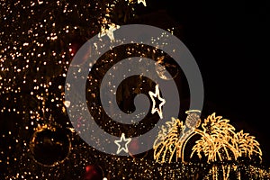 An image featuring an illuminated angel in the background, with a decorated branch of ornaments in the foreground for Christmas photo