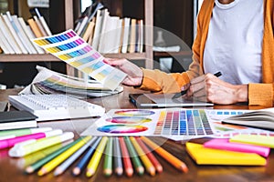 Image of female creative graphic designer working on color selection and drawing on graphics tablet at workplace with work tools