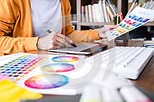Image of female creative graphic designer working on color selection and drawing on graphics tablet at workplace with work tools