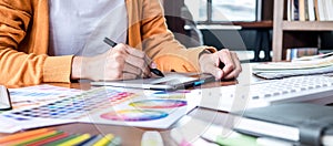 Image of female creative graphic designer working on color selection and drawing on graphics tablet at workplace with work tools