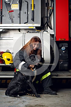 Image of female firefighter with black dog sitting on background of fire truck