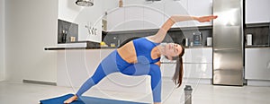Image of fit young woman doing workout, stretching her body, doing fitness, aerobics workout on yoga mat, standing in