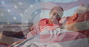 Image of flag of united states of america over senior biracial couple in deckchairs on beach