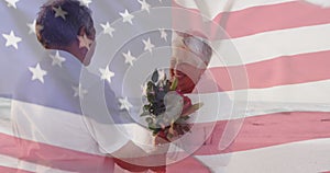 Image of flag of united states of america over senior biracial couple with flowers on beach