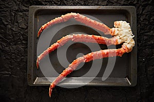 Image of fresh crab phalanges on oven-tray over dark background with copyspace photo